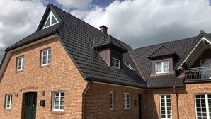 A two-story brick building with a steeply pitched roof, multiple windows, and a paved courtyard. - Ferienwohnung Herbstprinz (Stade)