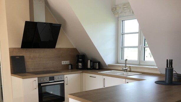 A modern kitchen with a central island, built-in oven, and a window providing natural light. - Ferienwohnung Herbstprinz (Stade)