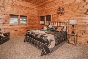 Quarto de cabana de madeira com cama, duas janelas, mesa de cabeceira e abajur.