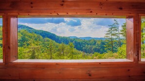 Una baita di legno con un'ampia finestra che si affaccia su un paesaggio montuoso boschivo.