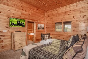 Un dormitorio de cabaña de madera con cama, cómoda, televisor y ventana.