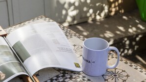 Eine offene Zeitschrift auf einem Tisch mit Muster, zusammen mit einer weißen Tasse.