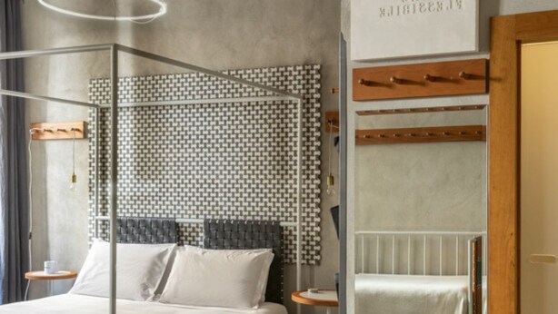 Ein Hotelzimmer mit Bett, Nachttisch, kleinem Tisch, Wandradiator und einer Wand mit Muster.