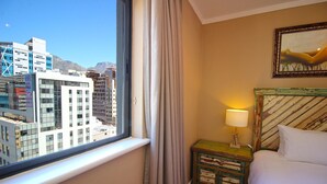 A hotel room with a large window, a bed, a bedside table with a lamp, and a painting on the wall. - Pristine Apartment in the Heart of Cape Town (Cape Town)
