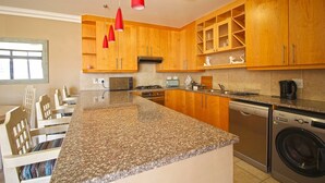 A kitchen with granite countertops, wooden cabinets, a dishwasher, and a red pendant light. - Pristine Apartment in the Heart of Cape Town (Cape Town)