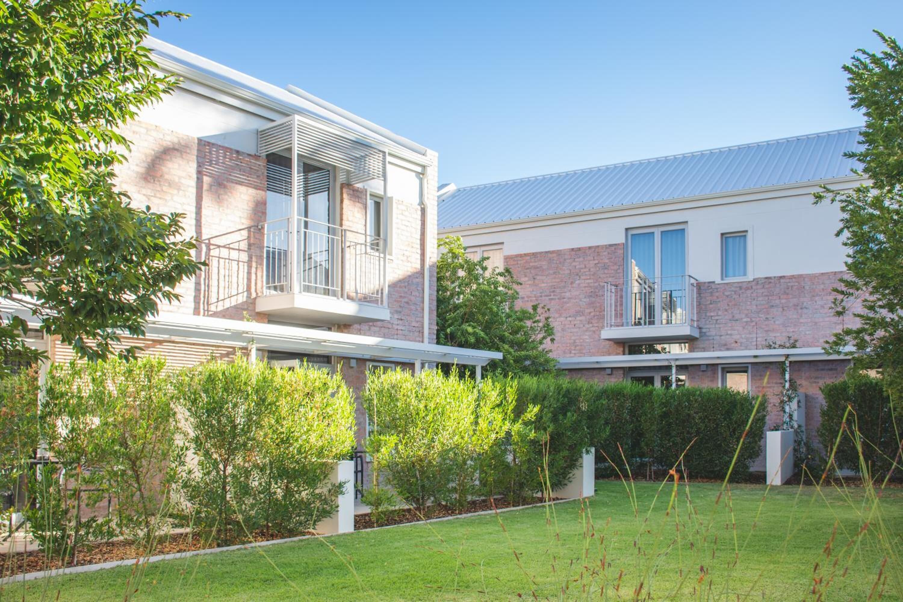 A modern two-story house with a balcony, brick facade, and a well-maintained lawn.