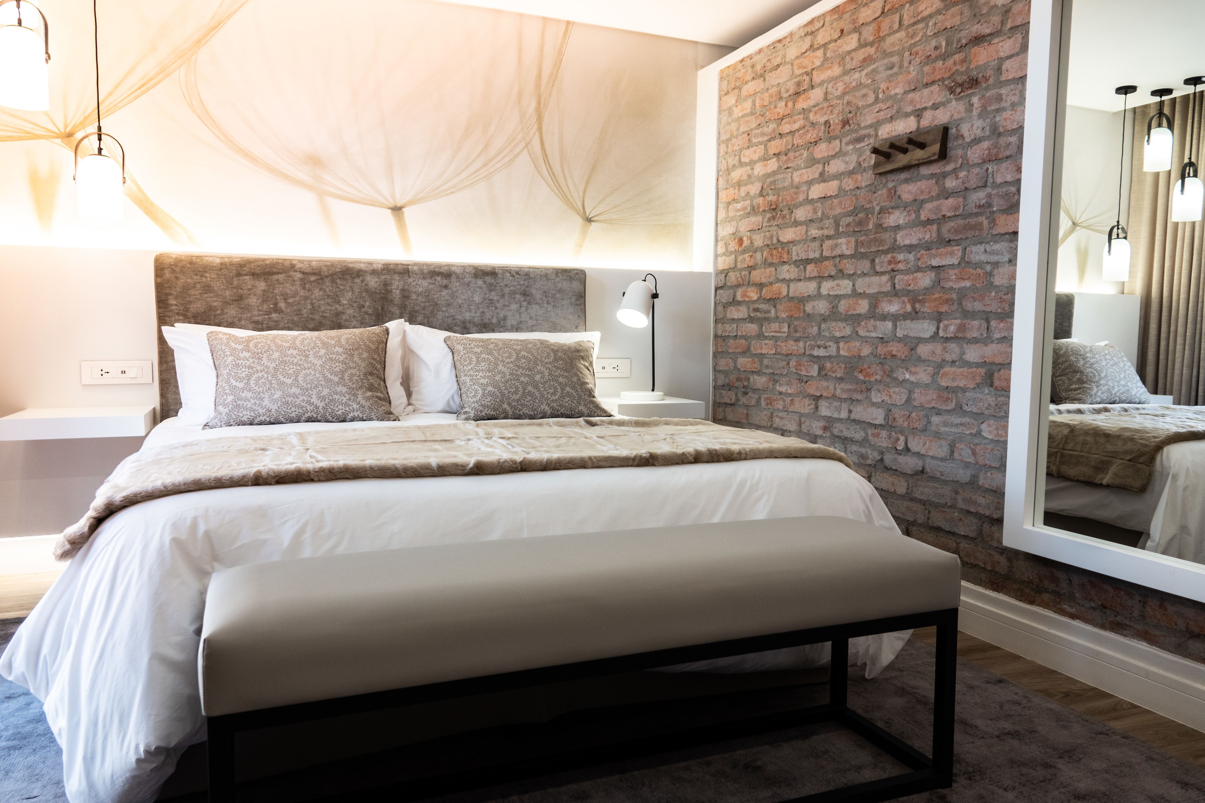 Ein modernes Schlafzimmer mit einer Ziegelwand, einem großen Spiegel und einem Bett mit vielen Kissen.
