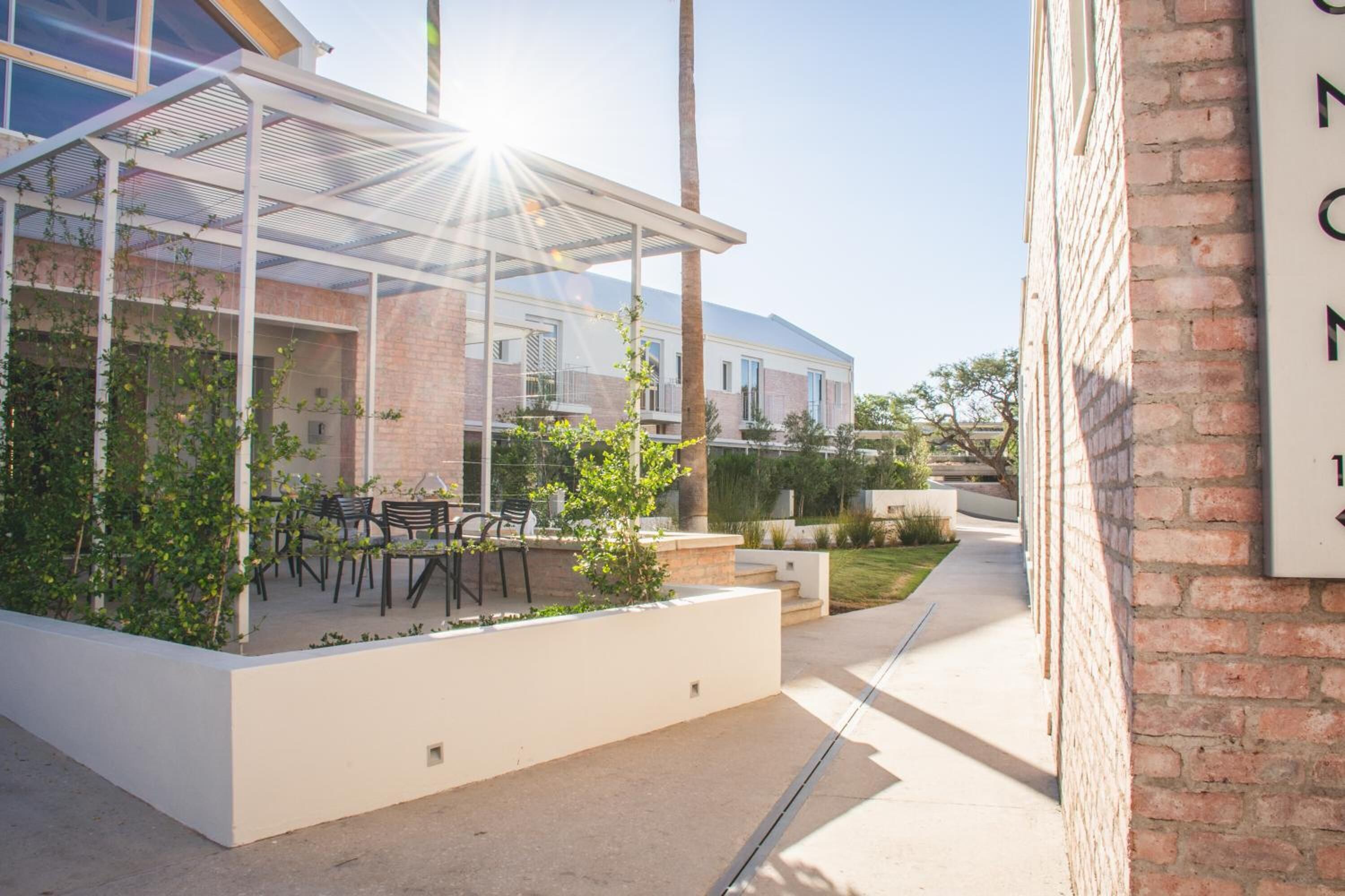Une terrasse extérieure moderne, dotée d’une véranda en verre, de sièges d’extérieur et d’un mur en briques.