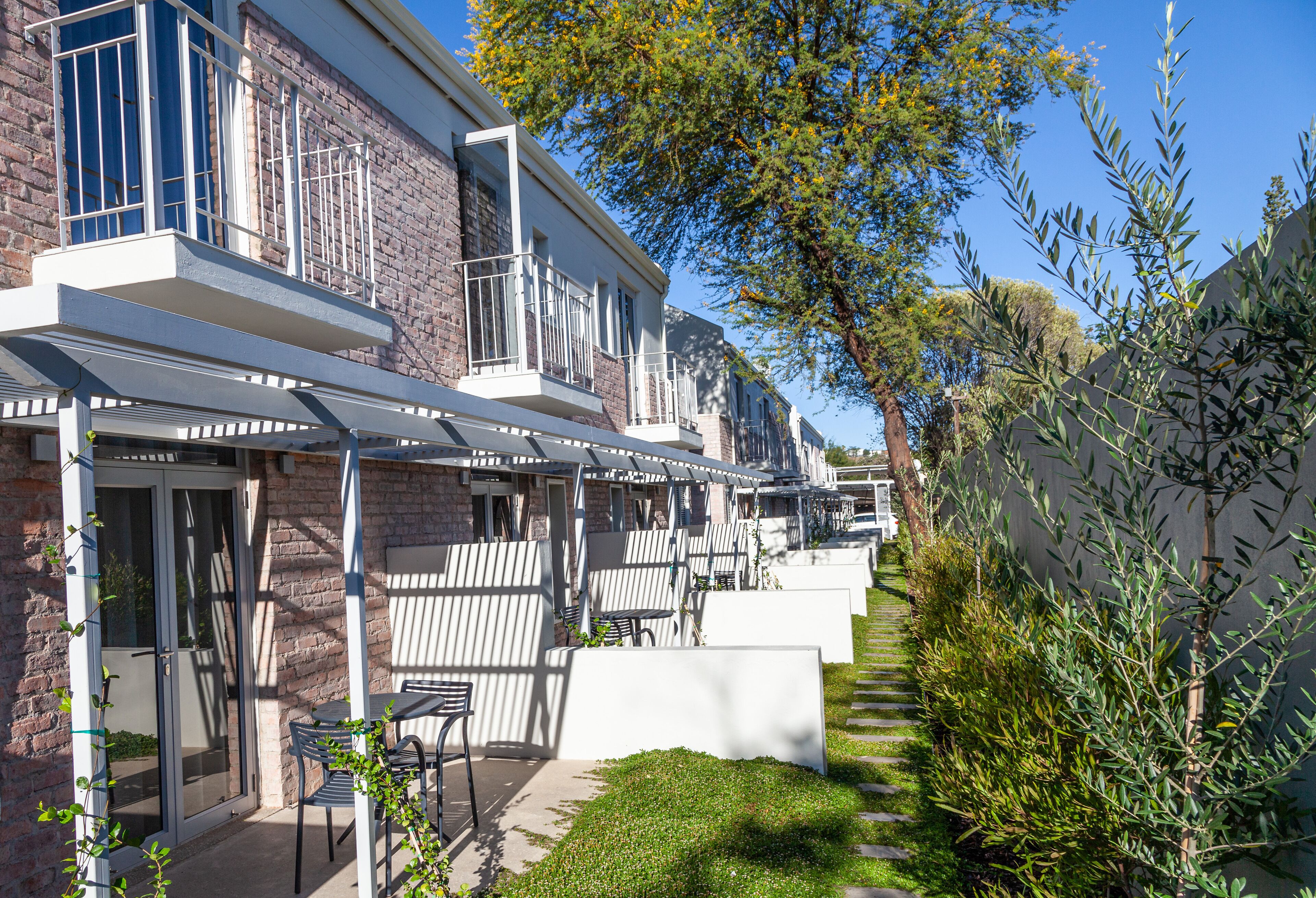 A row of modern townhouses with balconies, outdoor seating, and a well-maintained garden.