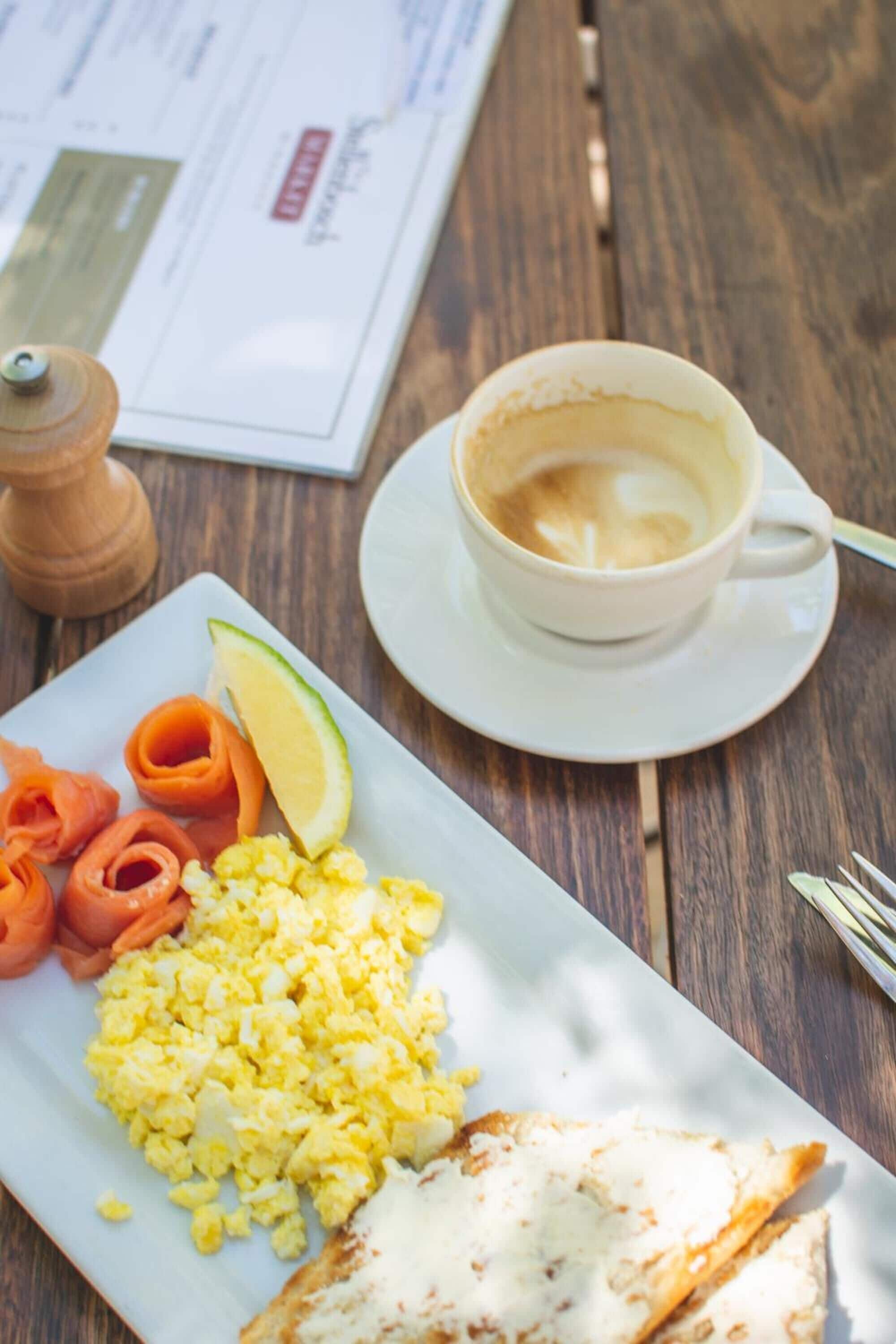 A breakfast plate with scrambled eggs, smoked salmon, and a slice of toast, accompanied by a cup of coffee on a wooden table.
