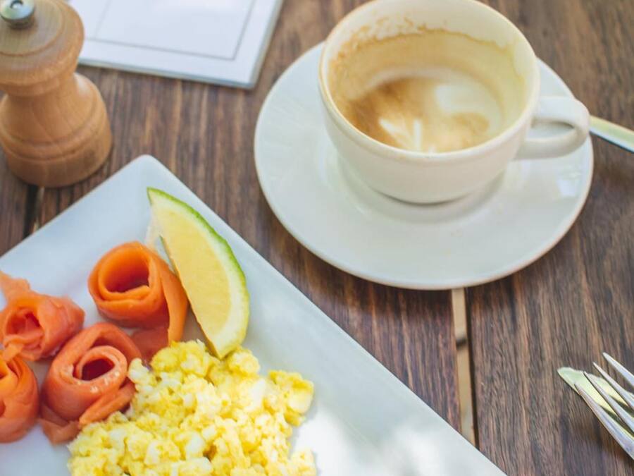 A breakfast plate with scrambled eggs, smoked salmon, and a slice of toast, accompanied by a cup of coffee on a wooden table.