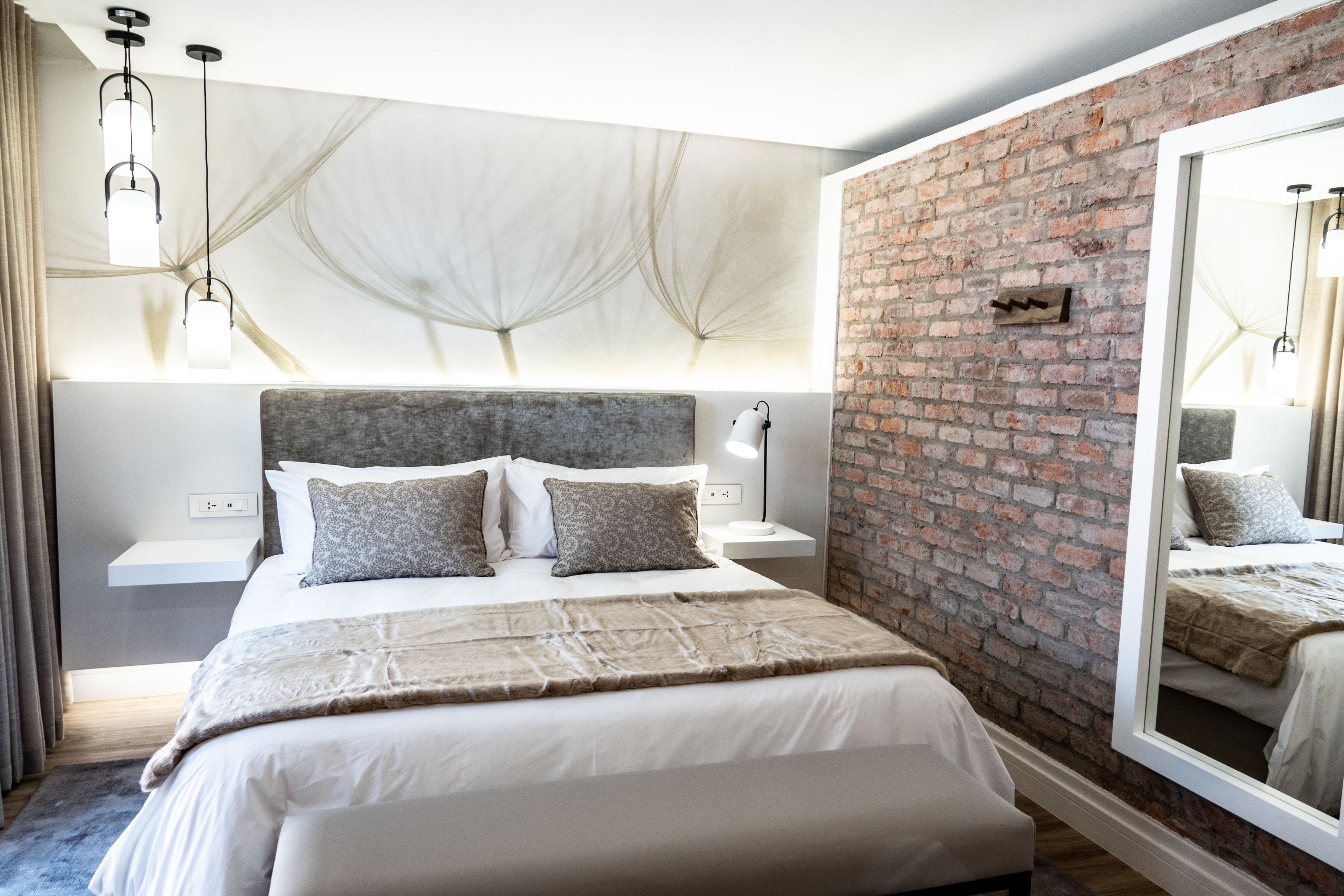 Een moderne slaapkamer met een groot bed, een accentmuur van baksteen, een wandplank en een grote spiegel.