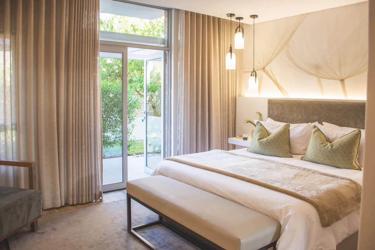 Ein Schlafzimmer mit einem großen Bett, einer Bank, einem Nachttisch und Blick ins Grüne.