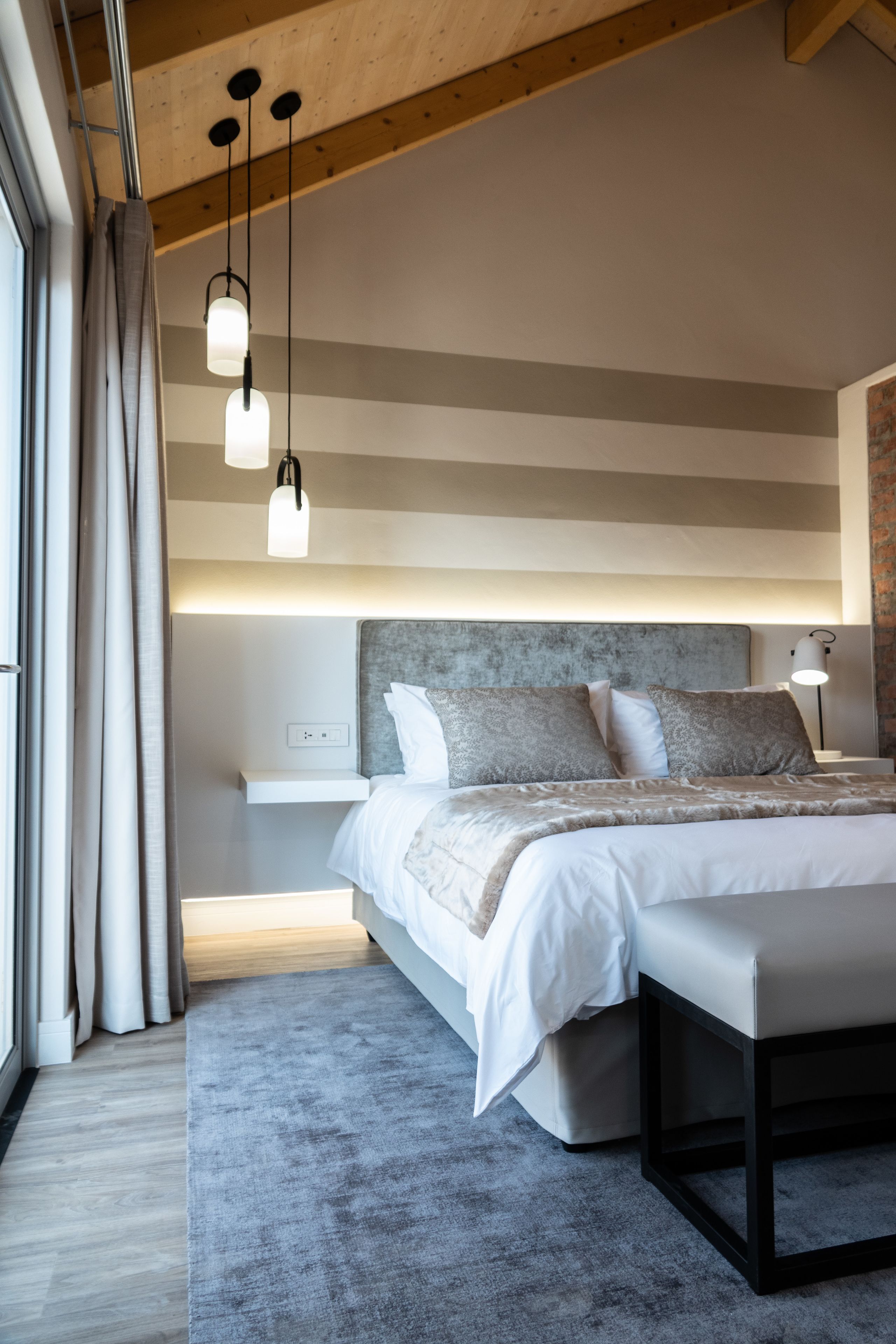 A modern bedroom with a large bed, bedside tables, and hanging pendant lights.