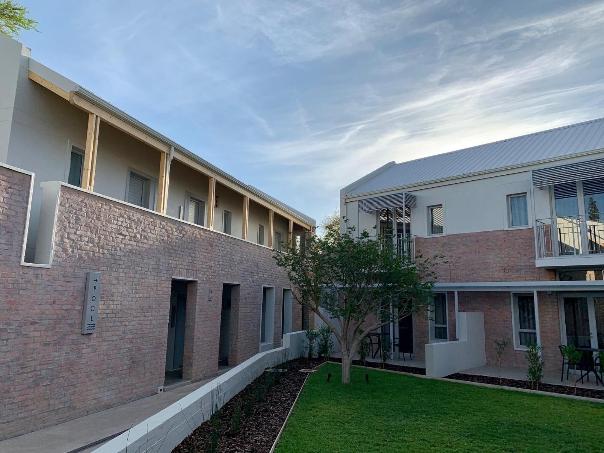 A modern building with a brick facade, multiple windows, and a small courtyard with a tree and outdoor seating.