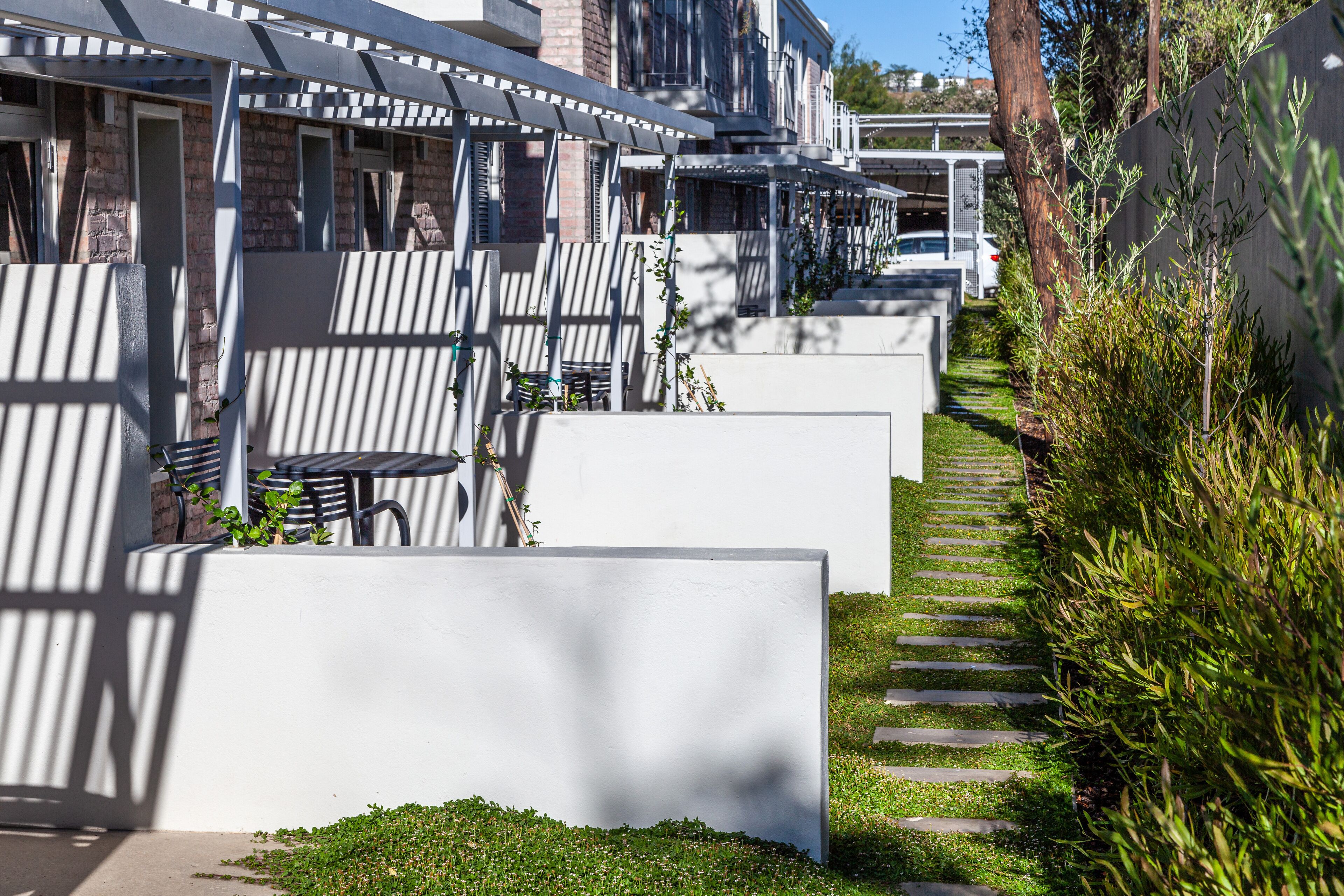 A row of modern, white-walled buildings with outdoor seating areas and a narrow pathway.