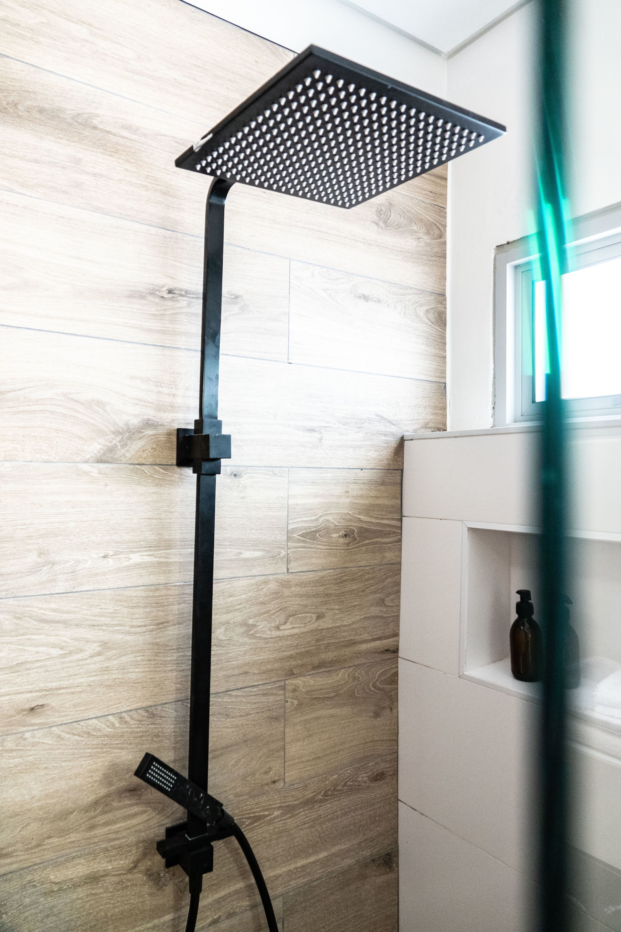A shower with a square head, a black stand, and a white tiled wall.
