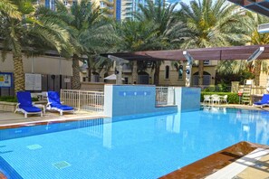 A swimming pool with blue tiles, surrounded by palm trees and lounge chairs.