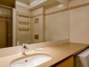 Ein Badezimmer mit Waschbecken, Spiegel, Handtuchhalter und Duschbereich.