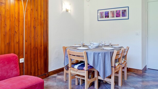 A dining area with a round table set for four, wooden chairs, a red sofa, and a wooden wall panel. - Modern 3-room apartment, ski-in, ski-out, La Tania, with parking (La Tania)