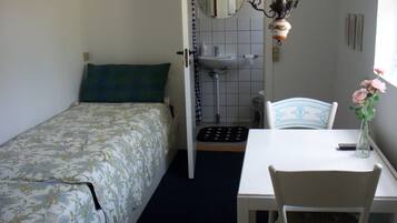 Une chambre à coucher comprenant un lit, une table de chevet, une chaise, une petite table, une lampe, un miroir, un lavabo et une fenêtre.