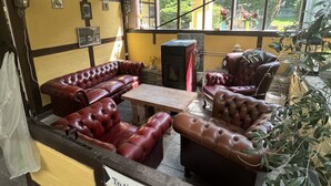 A cozy bar area with leather sofas and a wooden table, large windows offering a view of greenery, and a sign indicating the direction to the bar. - Danninghus (Svendborg)