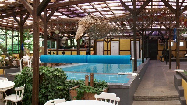 An indoor pool area with a covered roof, seating arrangements, and a bar.