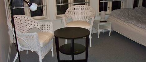 A room with a bed, two white wicker chairs, a small round table, and a floor lamp.
