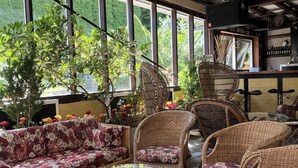 A covered outdoor seating area with wicker furniture and a glass table, surrounded by large windows offering views of greenery. - Danninghus (Svendborg)