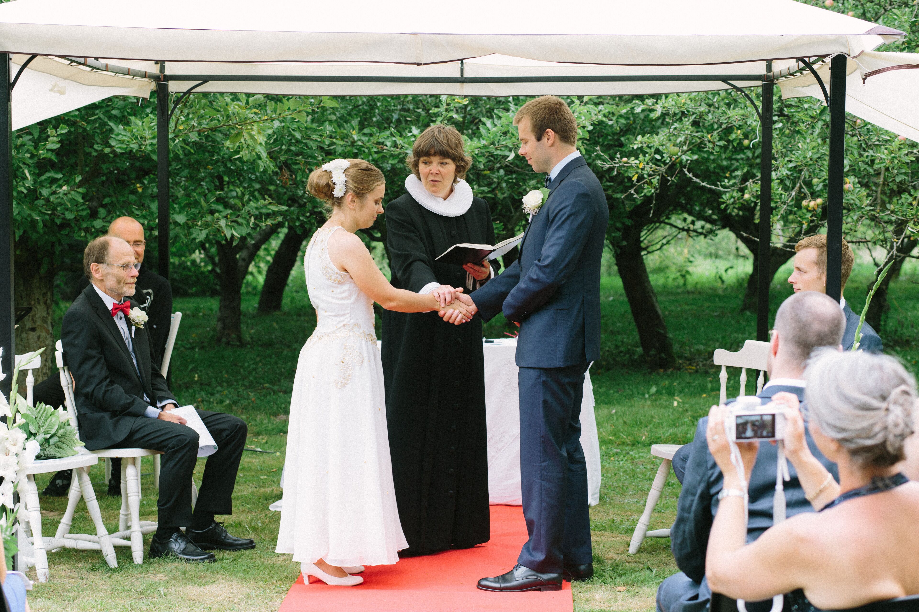 Una ceremonia de boda bajo una carpa, con invitados sentados en sillas y un fotógrafo capturando el evento.
