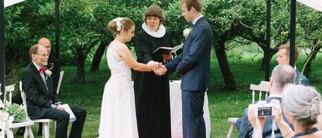 Una ceremonia de boda bajo una carpa, con invitados sentados en sillas y un fotógrafo capturando el evento.