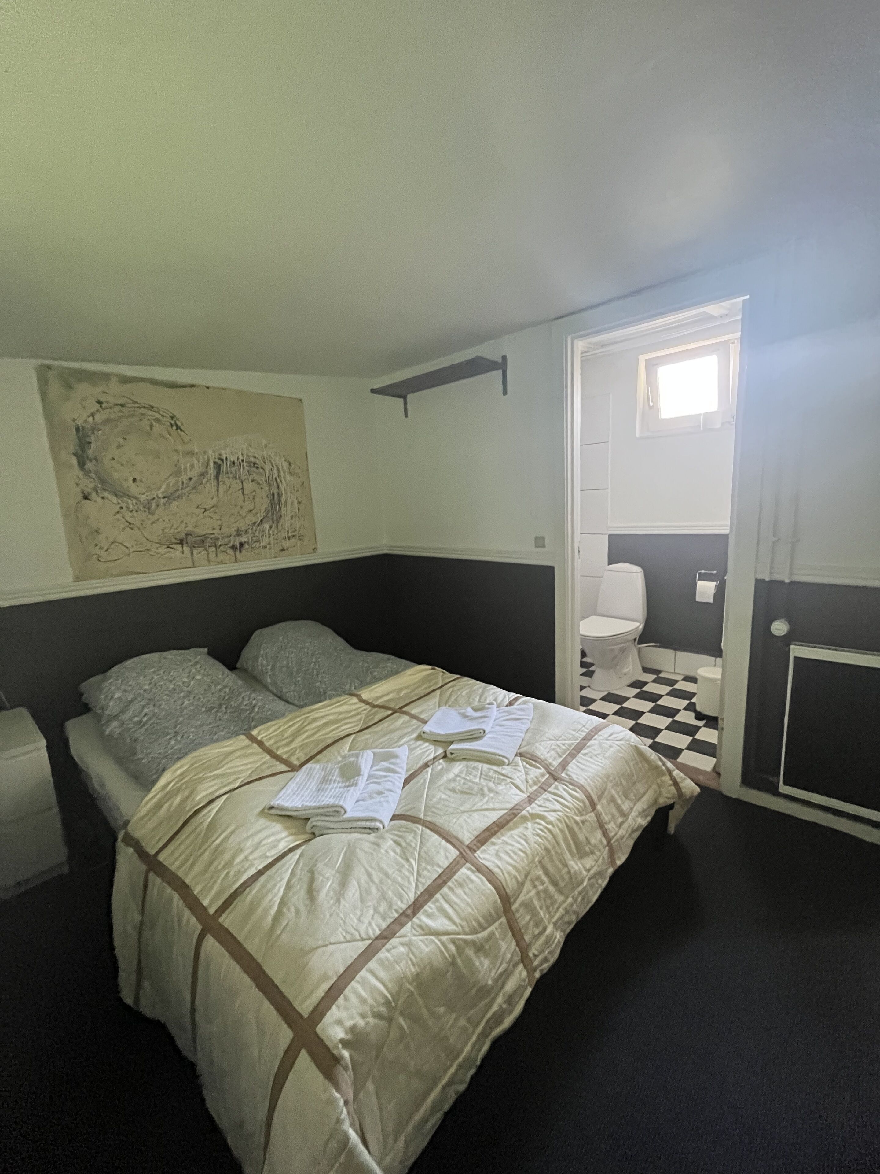 Un dormitorio con cama, una ventana pequeña, un inodoro y suelo a cuadros.