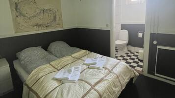 Un dormitorio con cama, una ventana pequeña, un inodoro y suelo a cuadros.