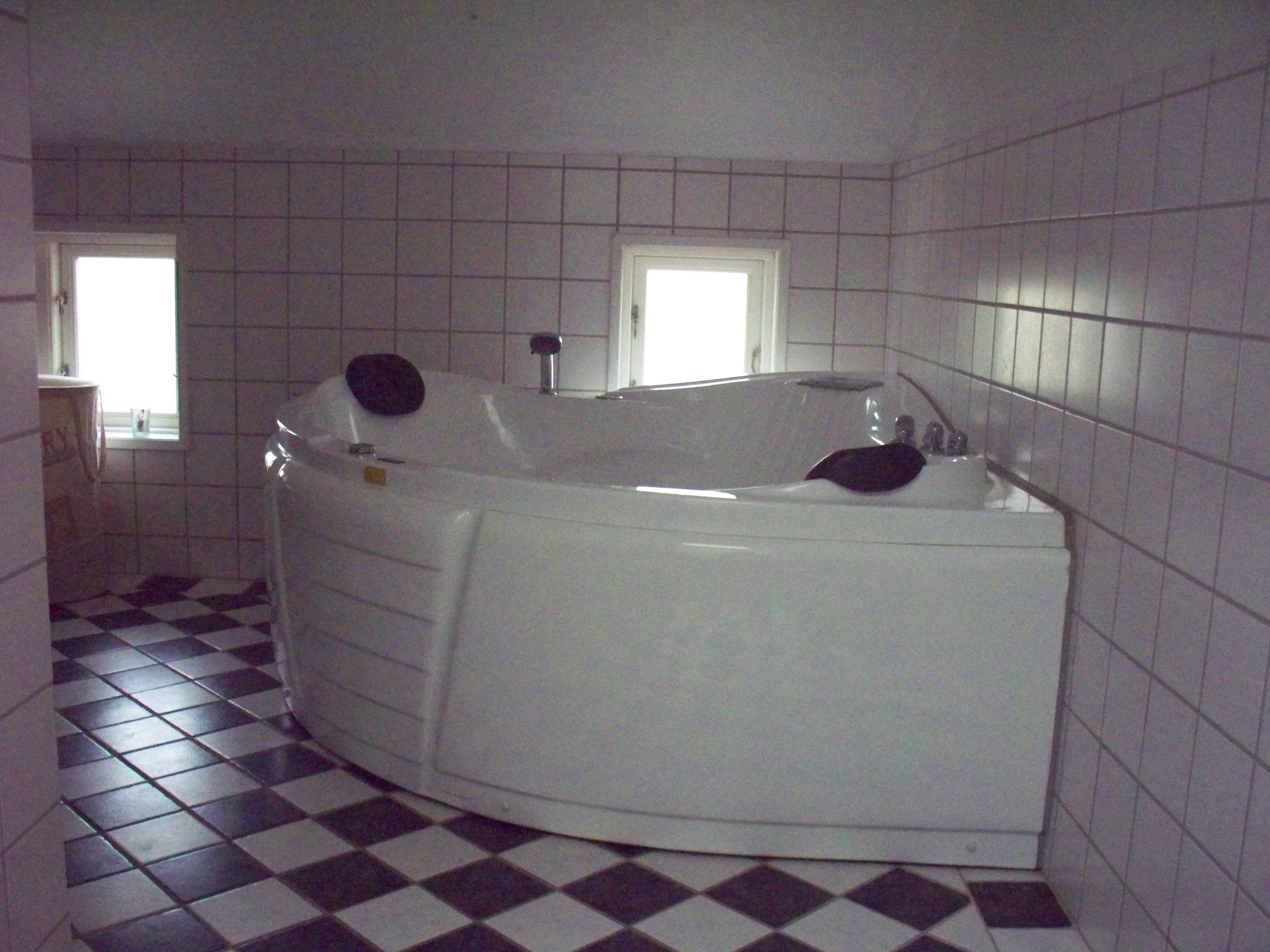 Une salle de bain avec une grande baignoire, un carrelage à motifs géométriques et des murs recouverts de carreaux blancs.