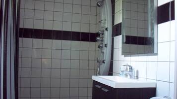 Une salle de bain avec des murs recouverts de carreaux blancs, une bande horizontale noire, un lavabo blanc avec un miroir au-dessus, et une douche au design incurvé.