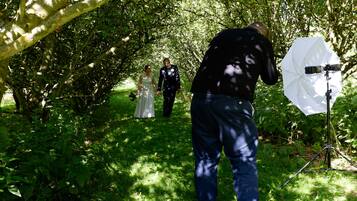 A wedding scene with a photographer and a couple walking through a lush, green forest.