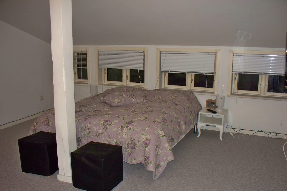 A bedroom with a bed, a nightstand, a lamp, and a window with blinds.