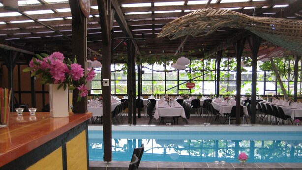 A restaurant with a pool, tables set for dining, and chairs. - Danninghus (Svendborg)