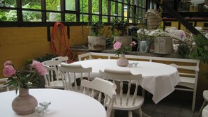 A restaurant with white tables and chairs, surrounded by potted plants and flowers.