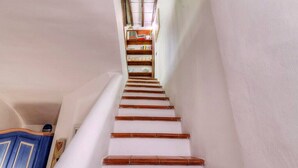 Una escalera con paredes blancas y escalones de madera que conduce a un rellano con un mueble azul y un cuadro enmarcado.