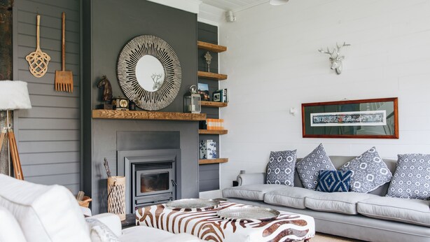 Un salon avec une cheminée, un ensemble de canapés, un pouf à motifs zébrés et des objets décoratifs disposés sur des étagères.