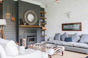 Ein Wohnzimmer mit Kamin, einer Sofagarnitur, einem Hocker mit ZEBRA-Muster und Dekorationen auf Regalen.