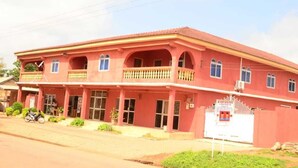 A two-story building with a red facade, multiple windows, and a balcony on the upper floor. - Hamasei Hotel (Kintampo)