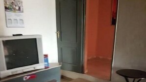 A room with a television on a stand, a door, a small table, and a few framed pictures on the floor. - Hamasei Hotel (Kintampo)