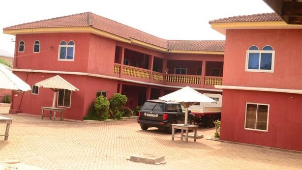 A red building with a tiled roof, a covered outdoor seating area, and a parked SUV. - Hamasei Hotel (Kintampo)
