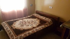 A small, single-bed room with a floral-patterned bedspread, a wooden headboard, and a small table with a cloth. - Hamasei Hotel (Kintampo)