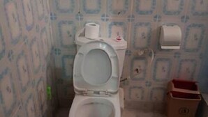 A bathroom with a toilet, a bidet, a toilet paper holder, and a trash bin. - Hamasei Hotel (Kintampo)