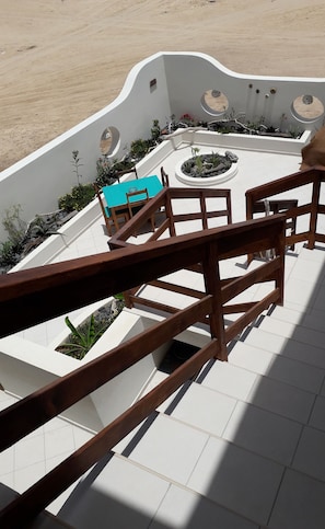 Ein sonniger Außenbereich mit einer Holztreppe zu einer Sitzecke mit einem türkisfarbenen Tisch und Stühlen.