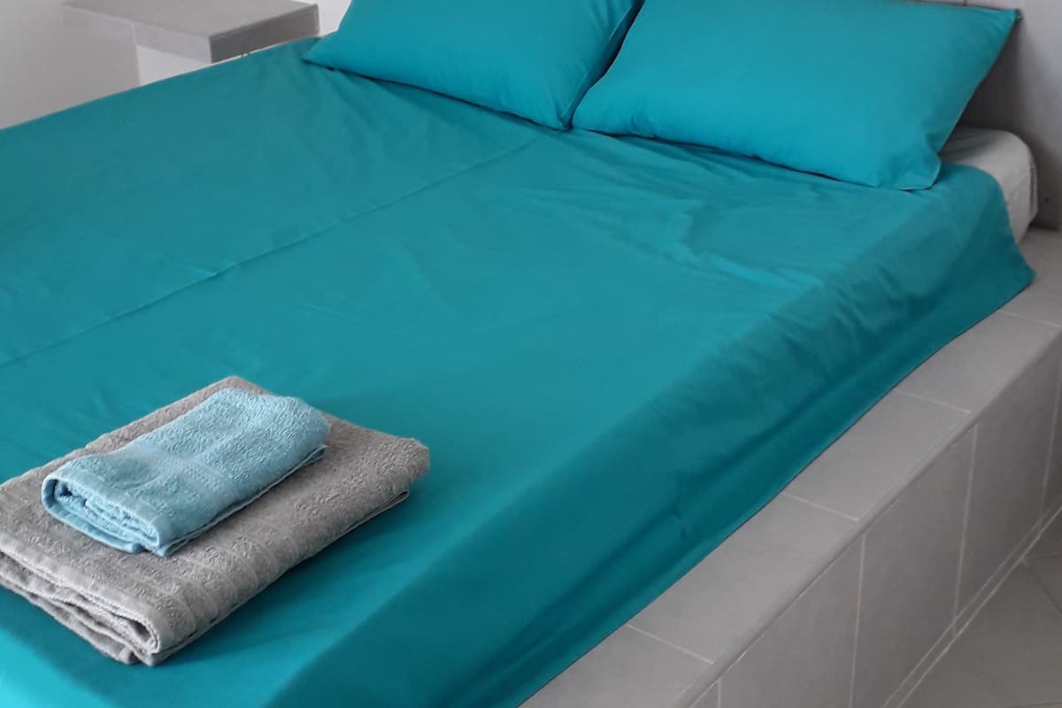 A bed with teal bedding, a grey headboard with circular cutouts, and a folded towel on the footboard.