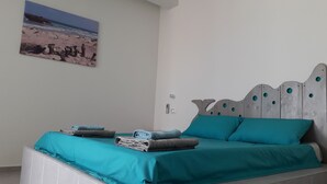 A bedroom with a bed, teal bedding, and a wall-mounted painting of a beach scene. - B&B Sereia Azul (Boa Vista)